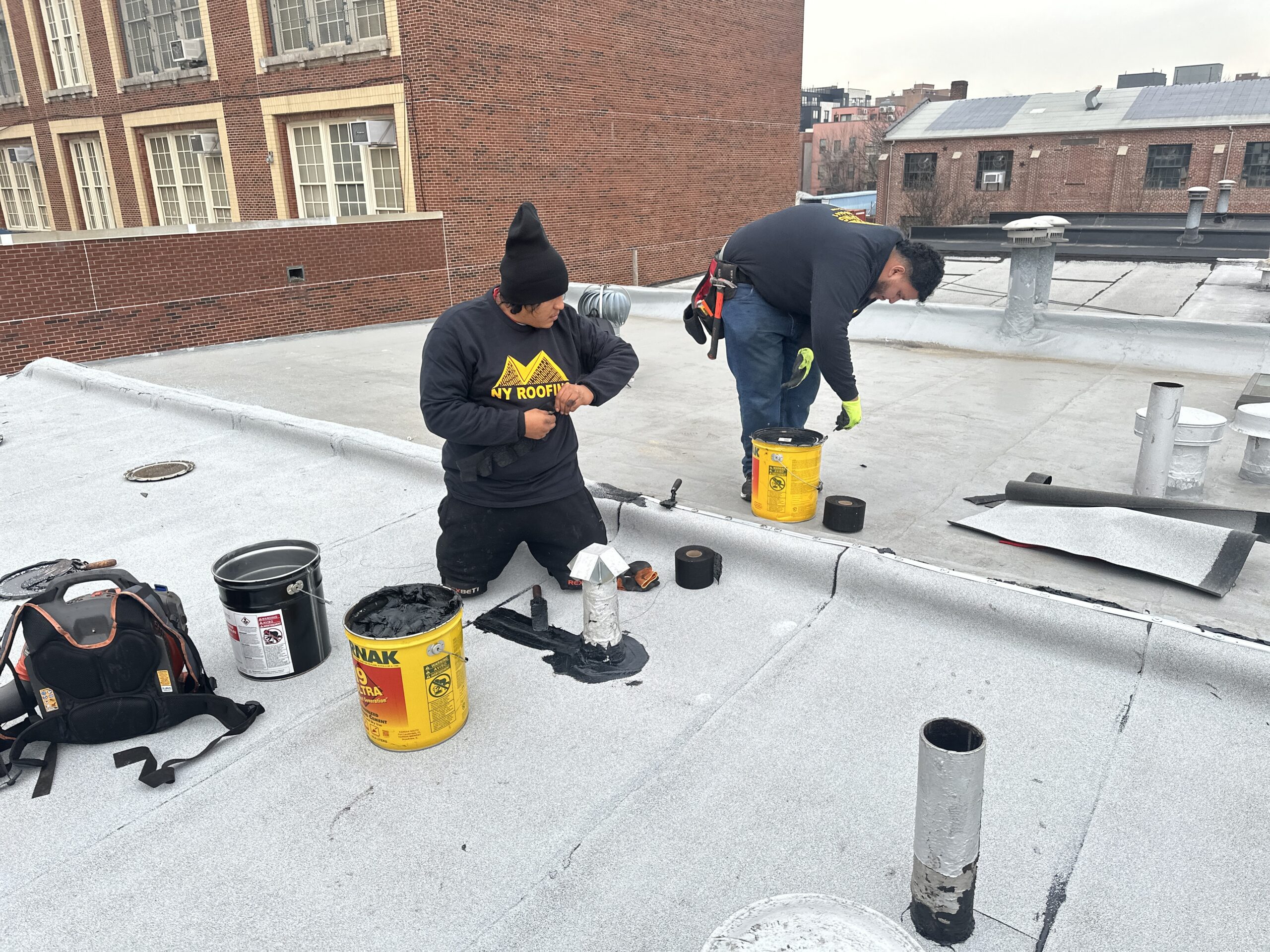 Commercial roof replacement NYC showing workers installing flat roofing system on large building